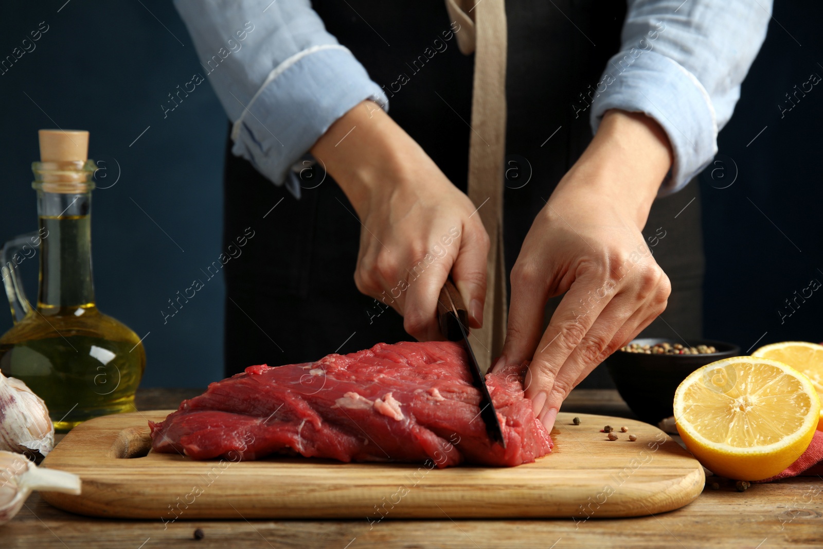 Photo of Woman cutting fresh raw meat at wooden table, closeup