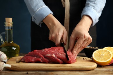 Woman cutting fresh raw meat at wooden table, closeup