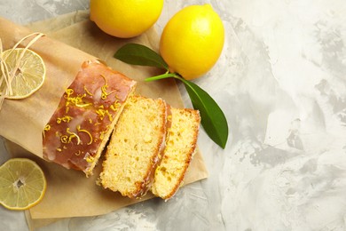 Cut tasty lemon cake with glaze and citrus fruits on light grey textured table, flat lay. Space for text