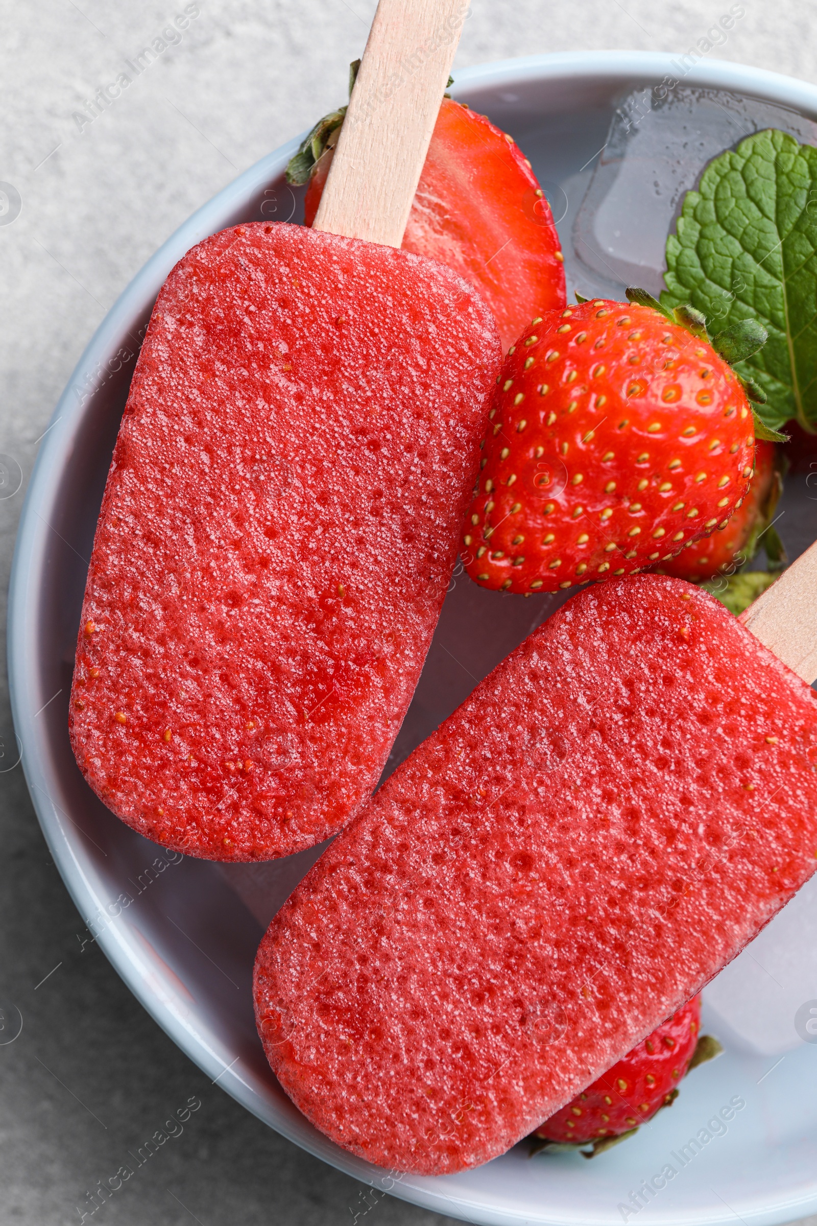 Photo of Bowl of tasty strawberry ice pops on grey table, top view. Fruit popsicle