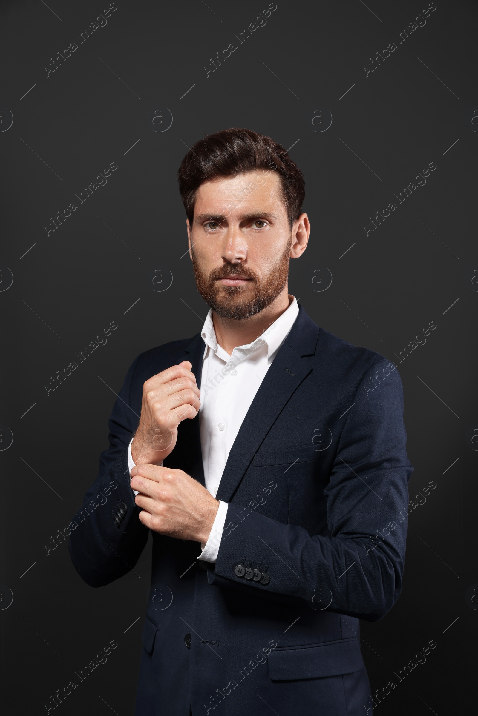 Photo of Handsome bearded man adjusting cufflinks on black background