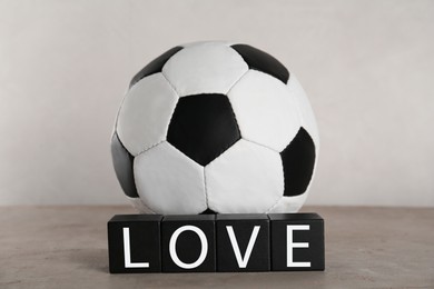 Photo of Soccer ball and cubes with word Love on grey table against light background