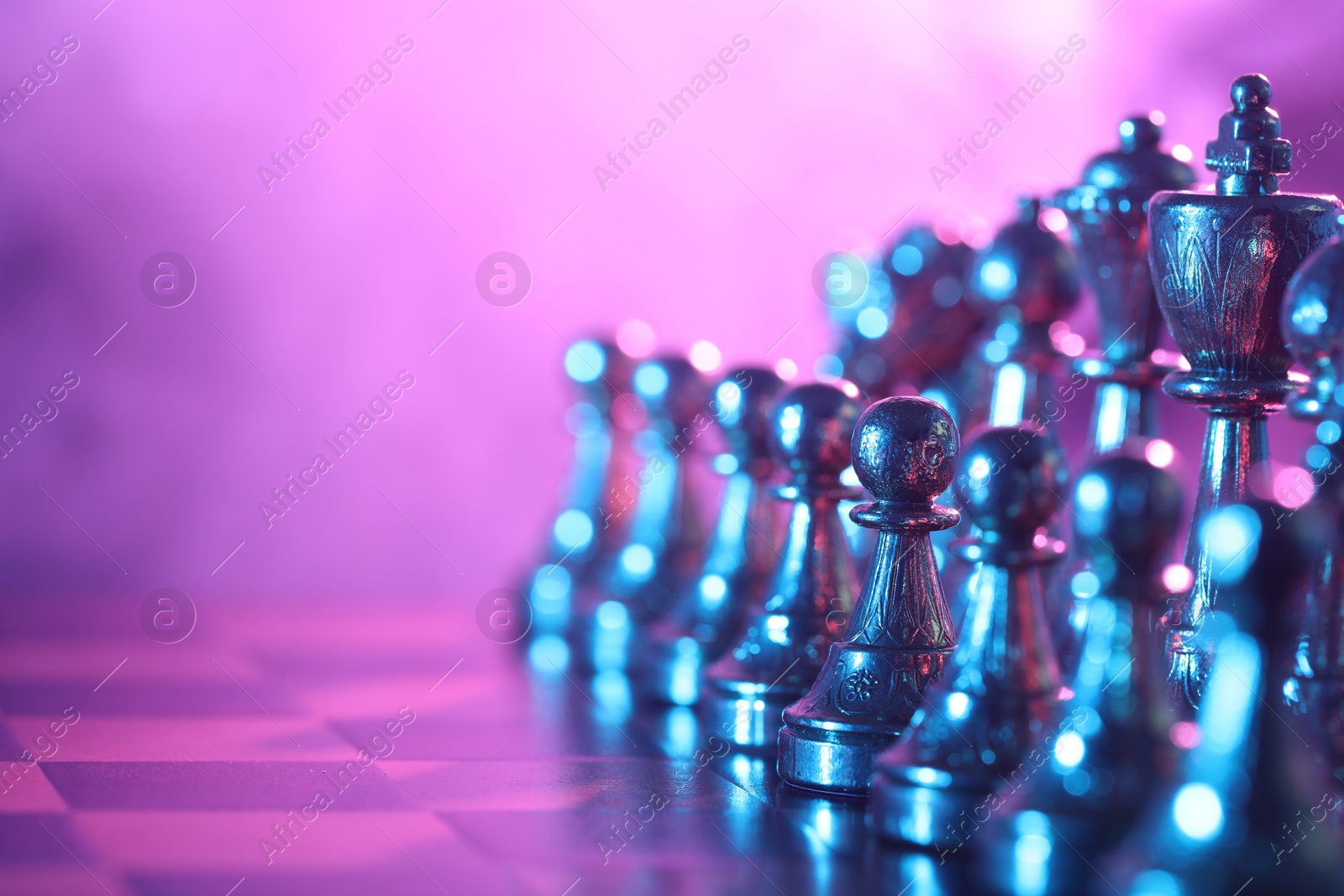 Photo of Chess pieces on checkerboard in color light, selective focus. Space for text