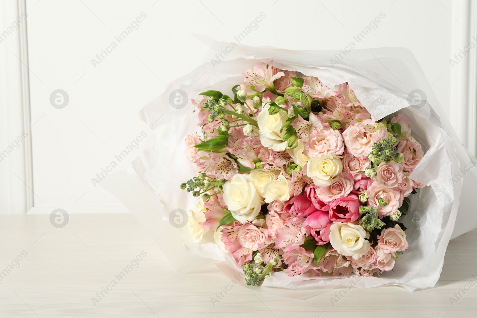 Photo of Beautiful bouquet of fresh flowers on wooden table near white wall, space for text