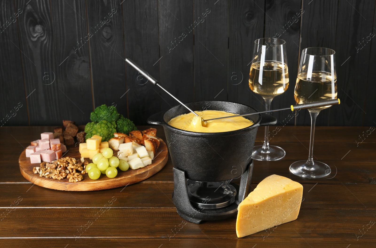 Photo of Fondue pot with melted cheese, glasses of wine and different products on wooden table