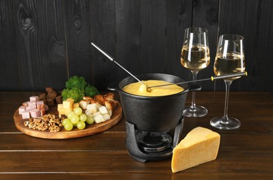 Photo of Fondue pot with melted cheese, glasses of wine and different products on wooden table