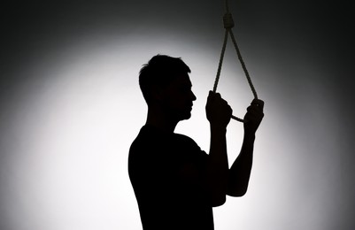 Photo of Silhouette of man with rope noose on light background