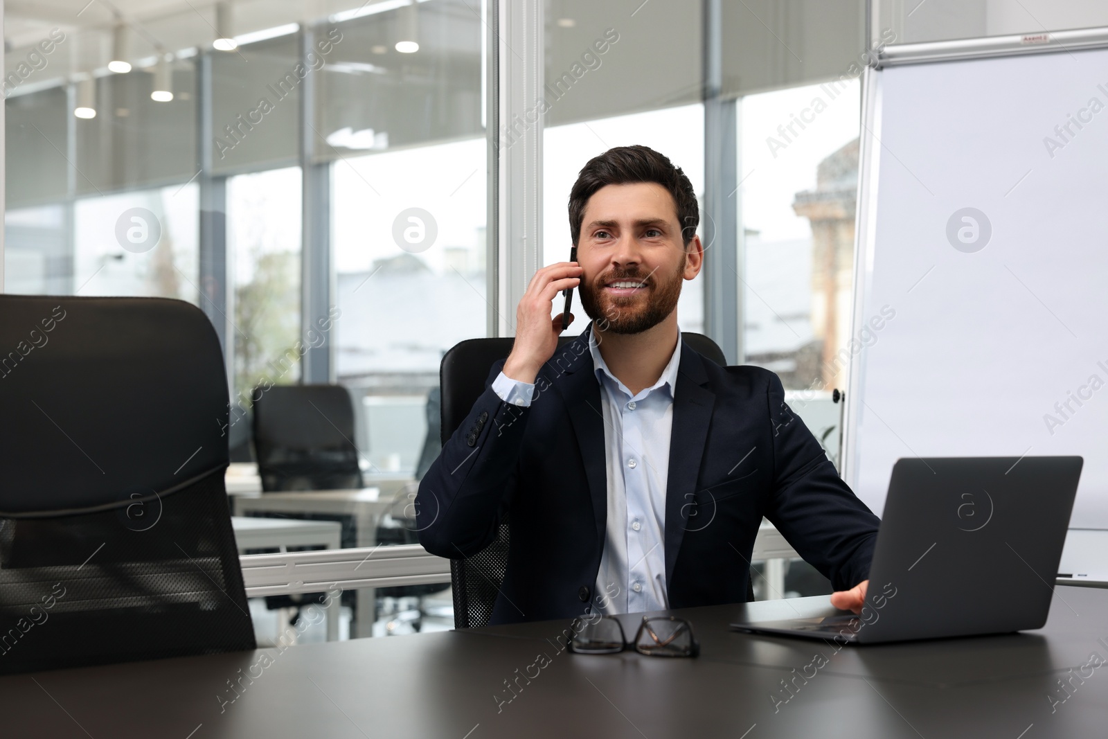 Photo of Man with laptop talking on phone at black desk in office