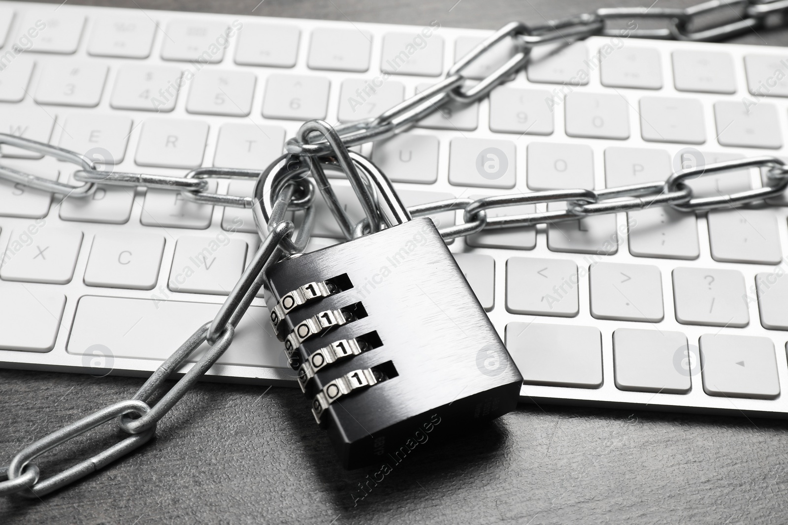 Photo of Cyber security. Metal combination padlock with chain and keyboard on grey table, closeup