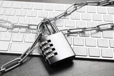 Cyber security. Metal combination padlock with chain and keyboard on grey table, closeup