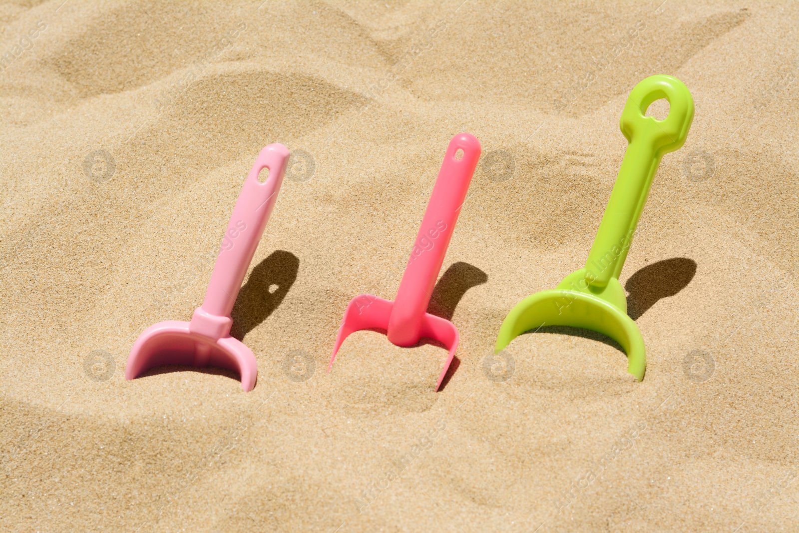 Photo of Bright plastic shovels in sand. Beach toys