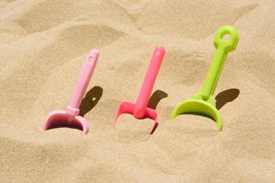 Photo of Bright plastic shovels in sand. Beach toys