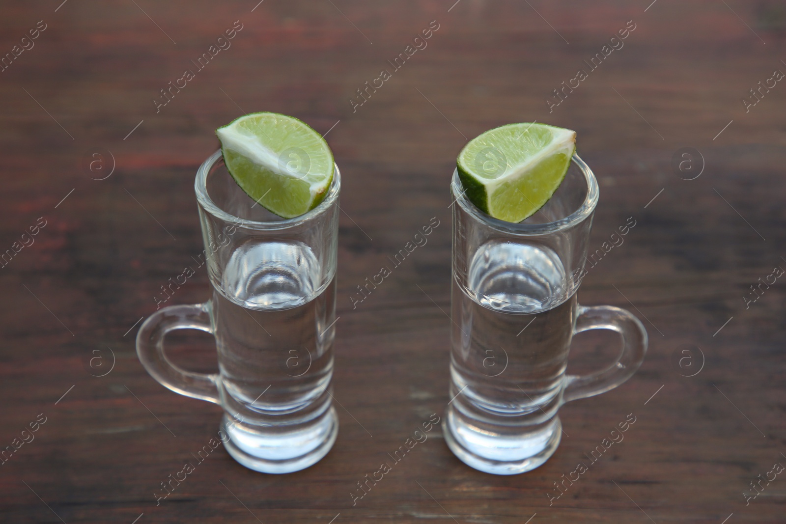 Photo of Mexican tequila shots with lime slices on wooden table