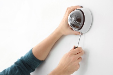 Technician installing CCTV camera on wall indoors, closeup