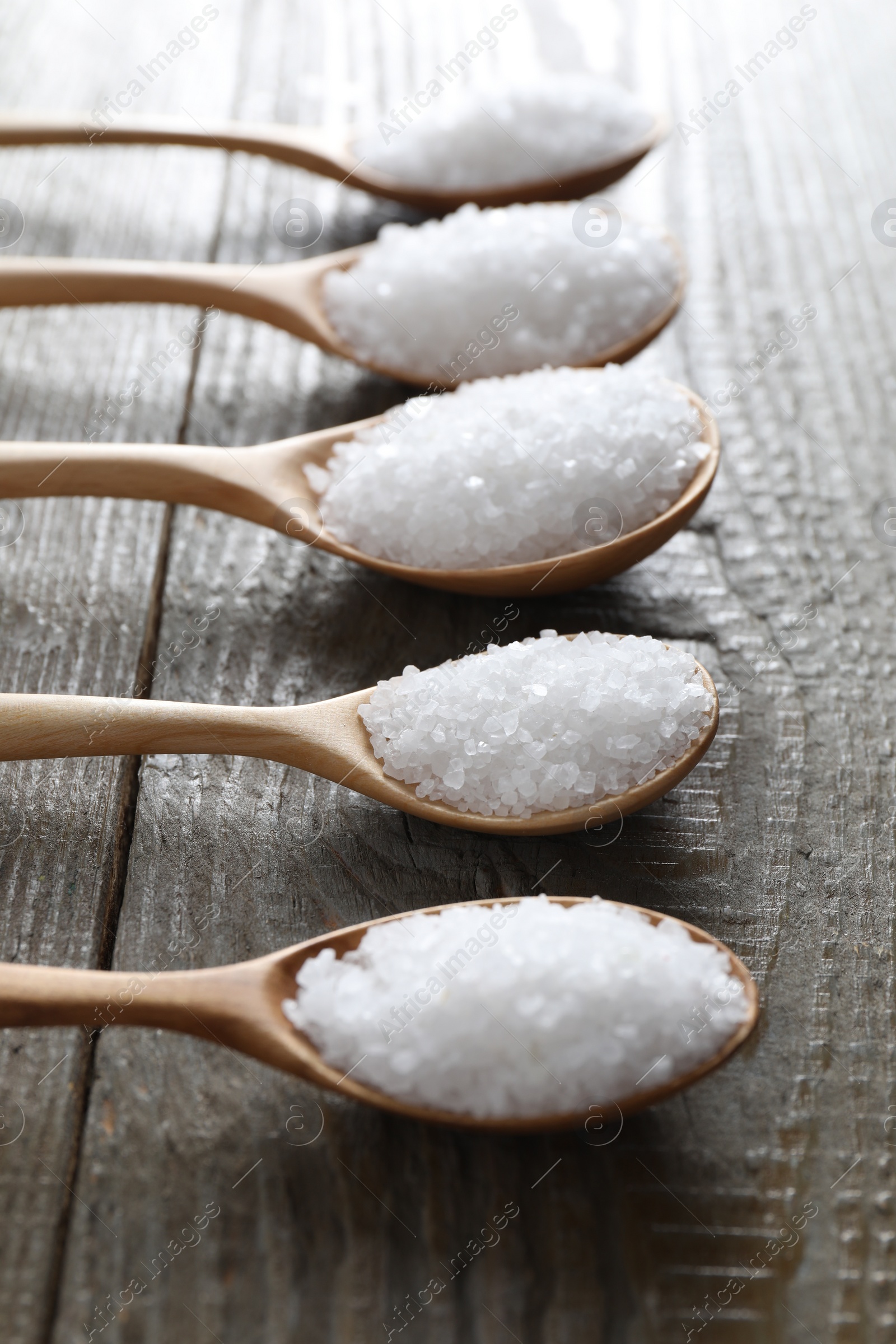 Photo of Organic salt in spoons on wooden table, closeup