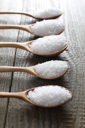 Photo of Organic salt in spoons on wooden table, closeup