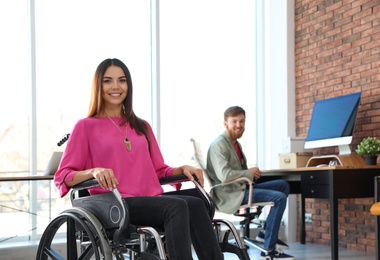 Photo of Young woman in wheelchair with colleague at office