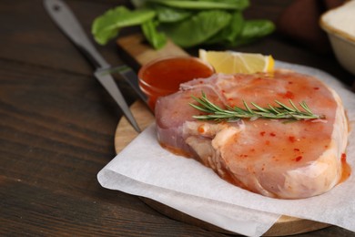 Photo of Board with raw marinated meat and rosemary on wooden table, closeup. Space for text