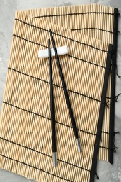 Photo of Bamboo mat with pair of black chopsticks and rest on table, top view