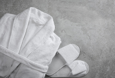 Photo of Clean folded bathrobe and slippers on grey stone background, flat lay