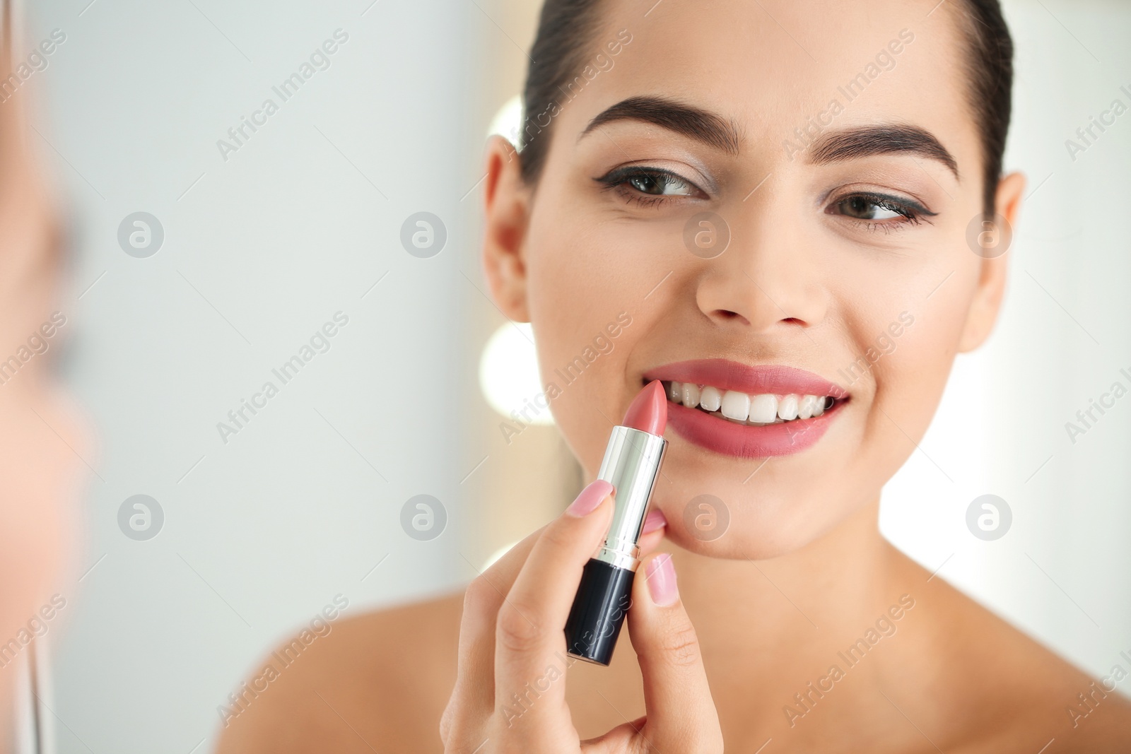 Photo of Young woman applying lipstick in front of mirror