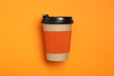 Photo of Takeaway paper coffee cup with cardboard sleeve on orange background, top view