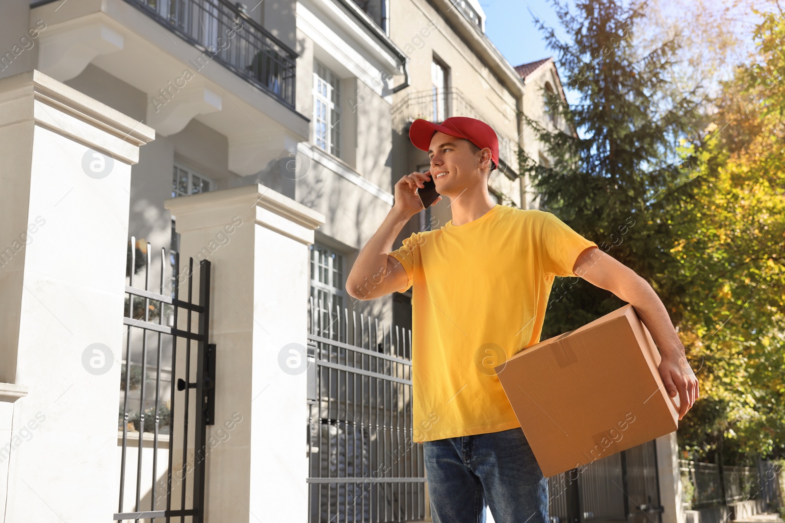 Photo of Courier with parcel talking by smartphone on city street