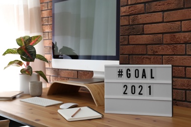 Photo of Light box with hashtag Goal 2021 near computer monitor on wooden desk in office