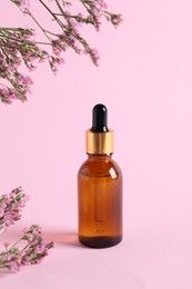 Bottle with cosmetic oil and flowers on pink background