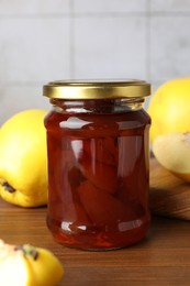 Tasty homemade quince jam in jar and fruits on wooden table