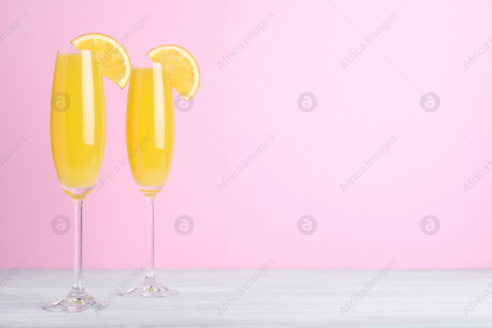 Photo of Fresh alcoholic Mimosa cocktails with orange slices on white wooden table, space for text