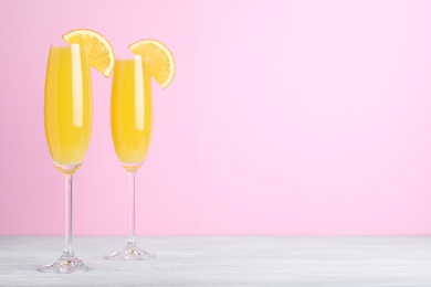 Fresh alcoholic Mimosa cocktails with orange slices on white wooden table, space for text