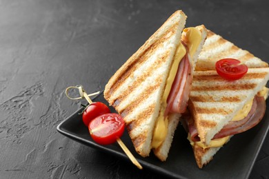 Photo of Tasty sandwiches with ham, melted cheese and tomatoes on black textured table, closeup