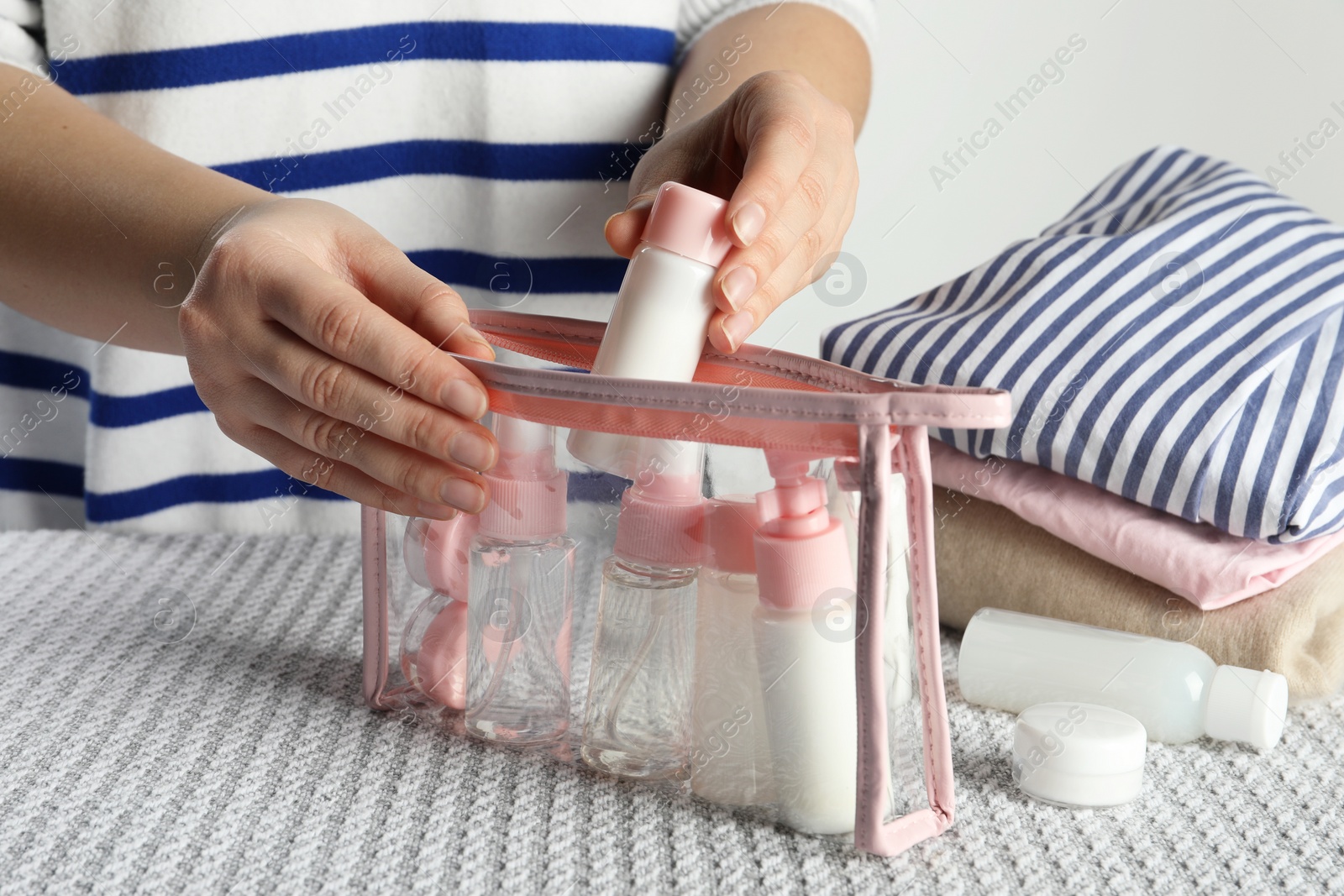 Photo of Woman putting small bottle with personal care product into plastic bag, closeup. Cosmetic travel kit