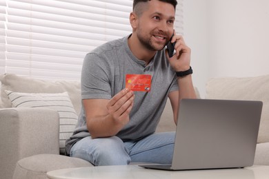 Handsome man with credit card using smartphone for online shopping at home