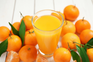 Glass of fresh tangerine juice and fruits on white wooden table