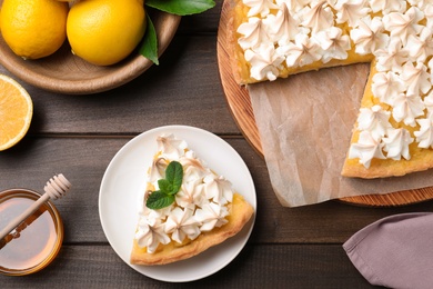 Photo of Cut delicious lemon meringue pie served on wooden table, flat lay