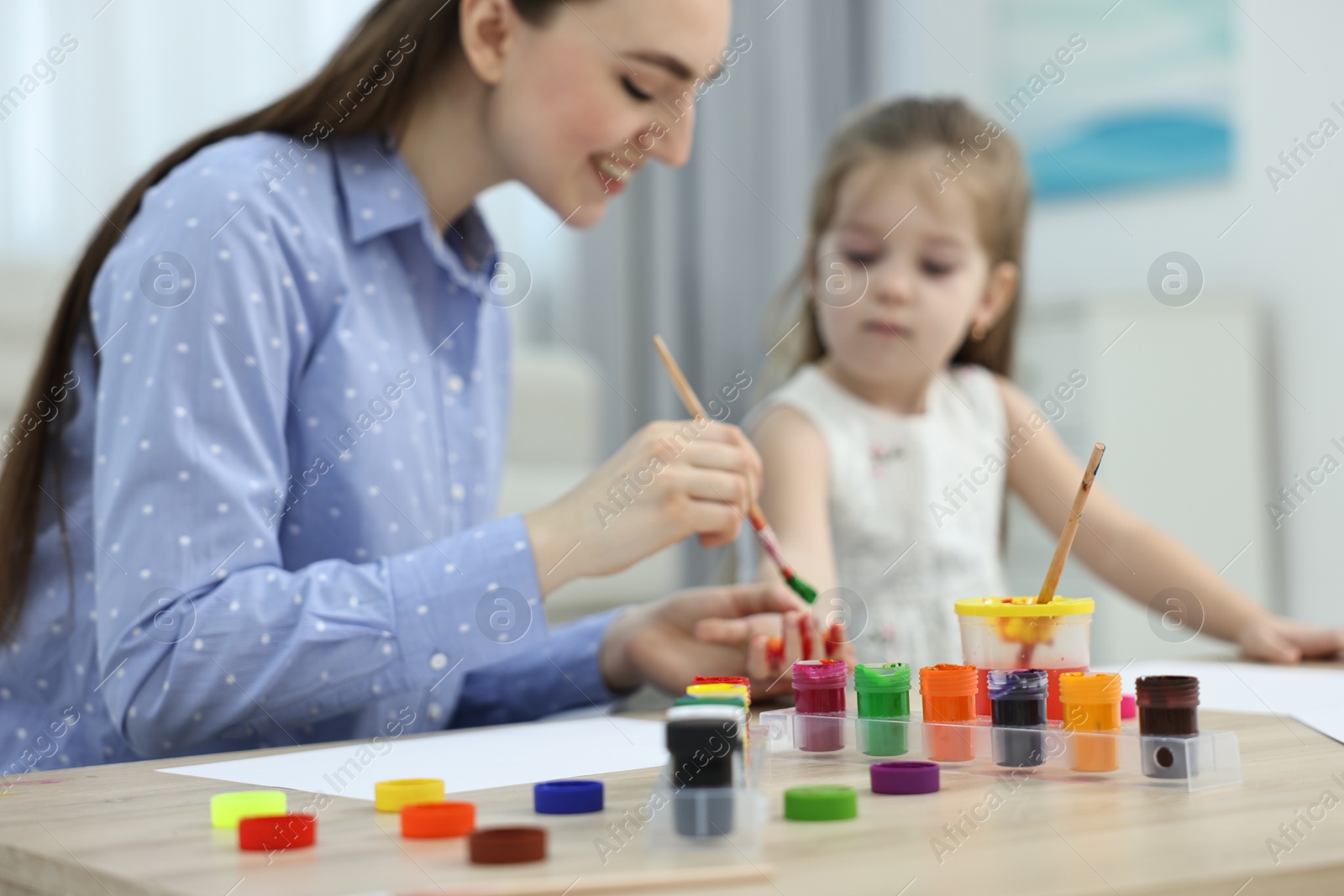 Photo of Mother and her little daughter painting with palms at home, selective focus
