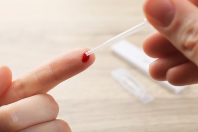 Laboratory testing. Woman taking blood sample from finger with pipette on blurred background, closeup