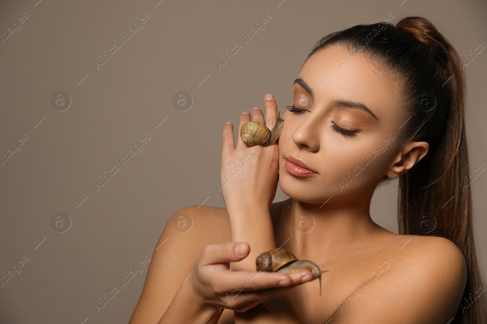 Photo of Beautiful young woman with snails on her hands against beige background. Space for text