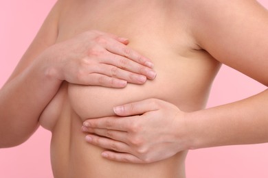 Photo of Mammology. Naked woman doing breast self-examination on pink background, closeup