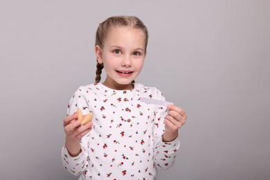 Photo of Cute girl holding tasty fortune cookie and reading prediction on light grey background