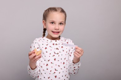 Cute girl holding tasty fortune cookie and reading prediction on light grey background