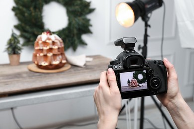 Photo of Food photography. Woman with professional camera taking photo of Pandoro cake, Christmas wreath and tree on table in studio, closeup. Space for text