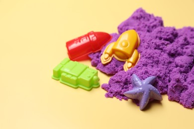 Photo of Violet kinetic sand and plastic toys on beige background, space for text
