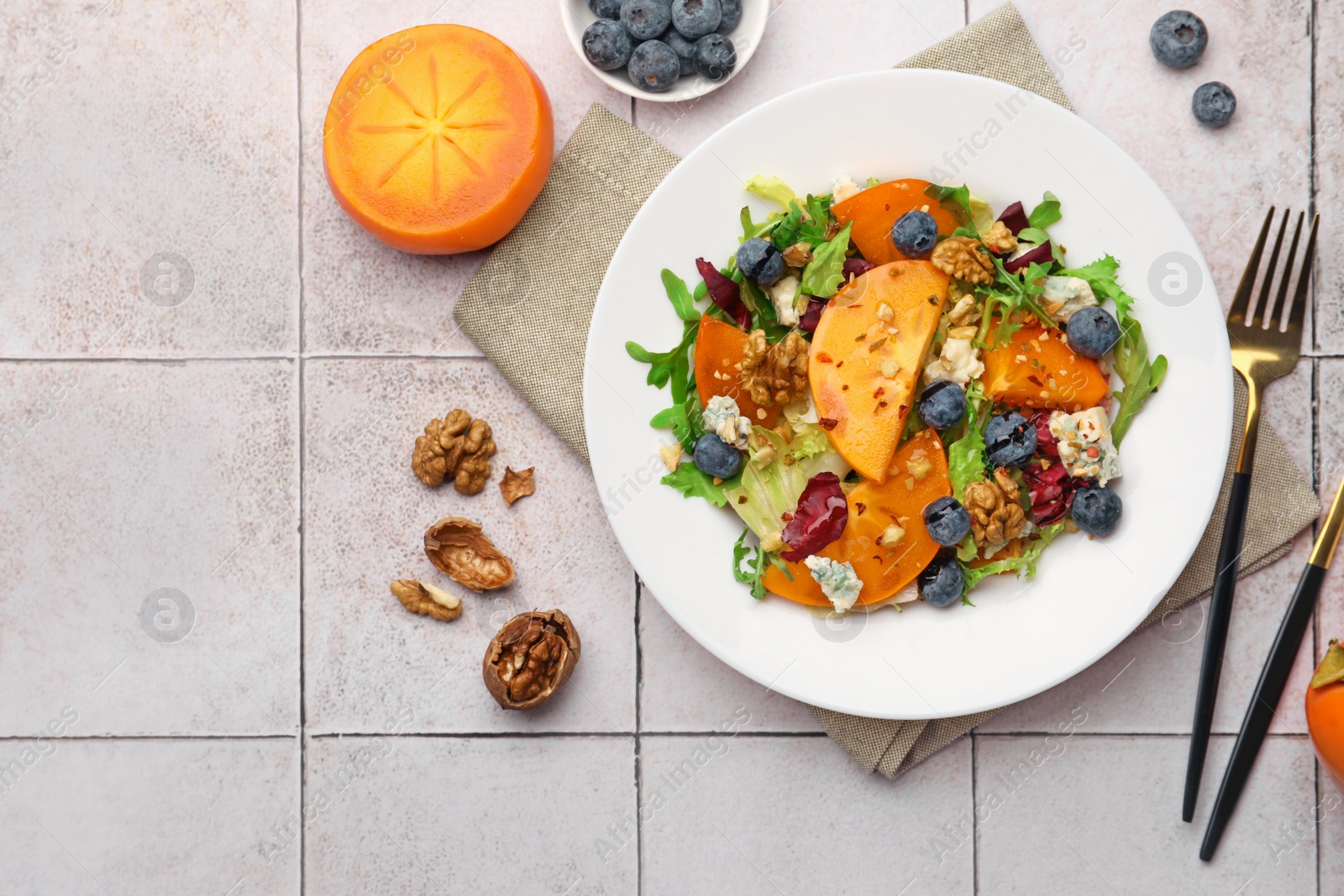 Photo of Delicious persimmon salad, fork and knife on tiled surface, flat lay. Space for text