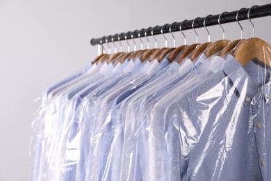 Hangers with shirts in dry cleaning plastic bags on rack against light background