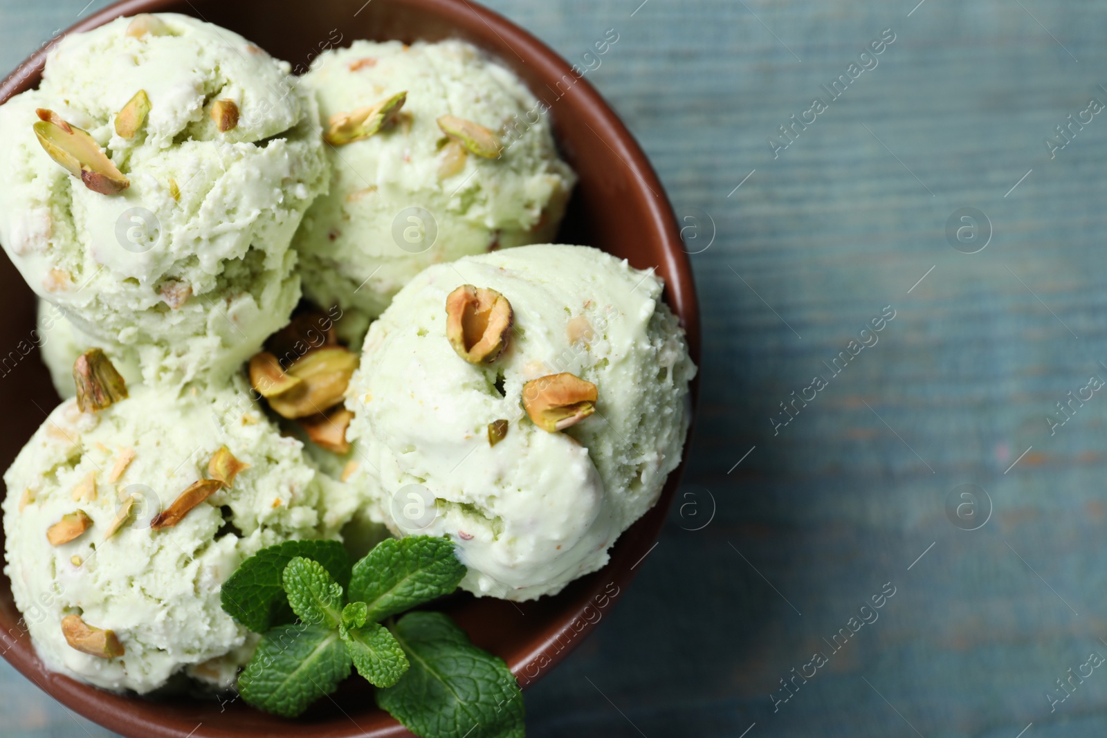 Photo of Delicious pistachio ice cream in bowl on blue wooden table, top view. Space for text