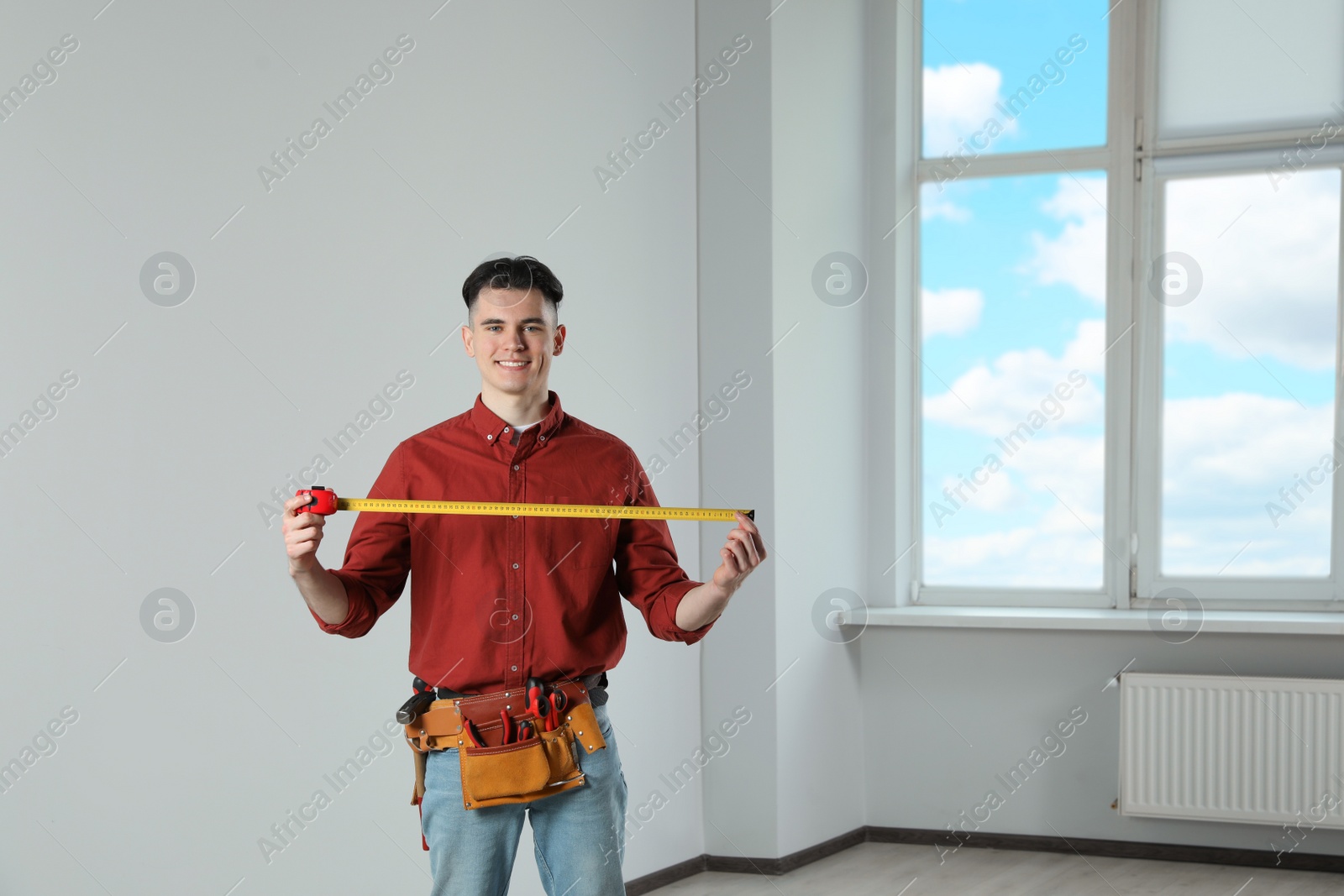 Photo of Handyman with tool belt and measuring tape in empty room
