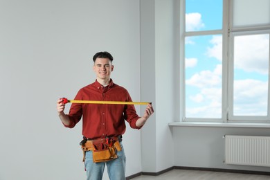 Photo of Handyman with tool belt and measuring tape in empty room